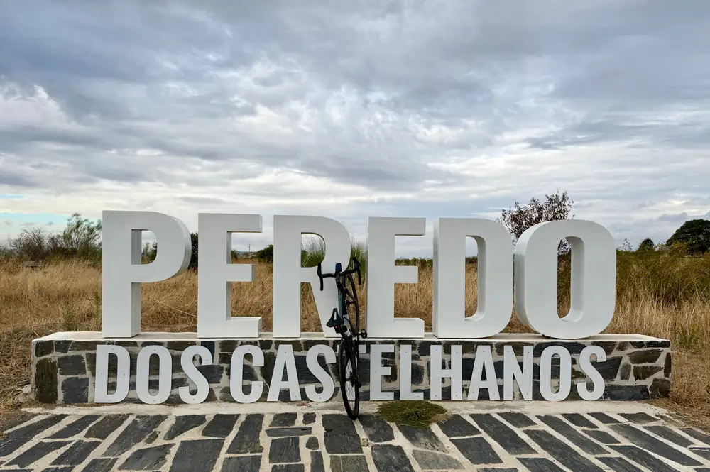 Letreiro com o nome Peredo dos Castelhanos sobre um muro de xisto, com uma bicicleta encostada